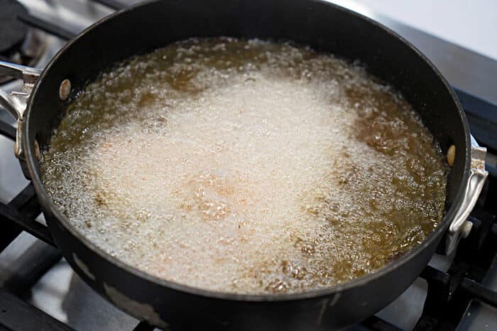 A black pan on a stove with fried tilapia deep frying in bubbling hot oil, perfect for your next tilapia recipe.