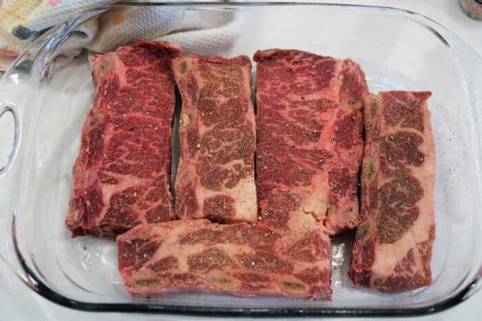 Raw, seasoned beef short ribs arranged in a glass baking dish, ready for cooking.