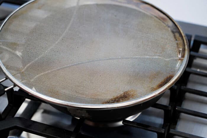 A frying pan on a stove, covered with a metal mesh splatter screen, is perfect for preparing your favorite fried tilapia recipe.
