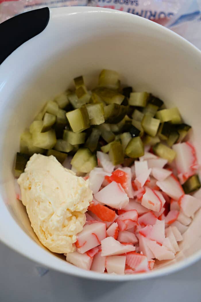 Chopped pickles, imitation crab meat, and mayonnaise in a white mixing bowl.