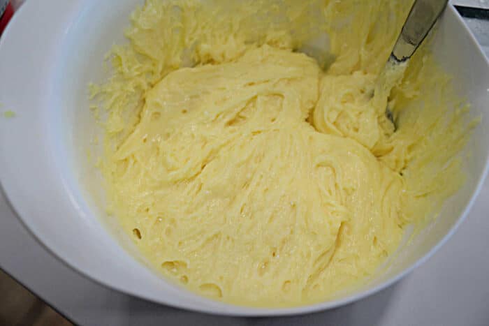 A white bowl filled with creamy yellow carnivore diet cake batter and a metal spoon partially dipped in.