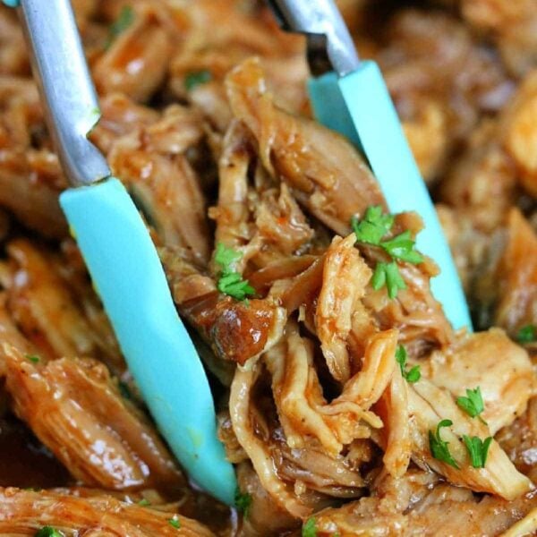 Tongs holding shredded barbecue chicken garnished with chopped parsley, served alongside tender Ninja Foodi pulled pork.
