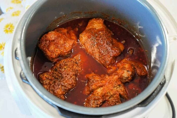 Four pieces of seasoned chicken simmering in red sauce inside a slow cooker, just as tender as classic Ninja Foodi pulled pork.