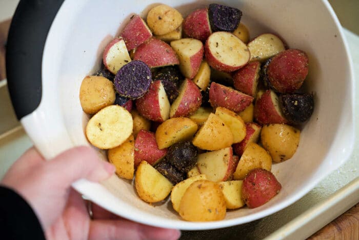 A bowl of seasoned, chopped red, yellow, and purple potatoes is ready for roasting&mdash;perfect to pair with shrimp and potatoes for a hearty meal.
