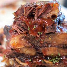 Close-up of stacked, juicy BBQ beef ribs with sauce and herbs on foil.
