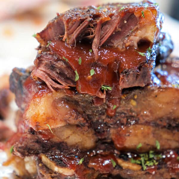 Close-up of stacked, juicy BBQ beef ribs with sauce and herbs on foil.