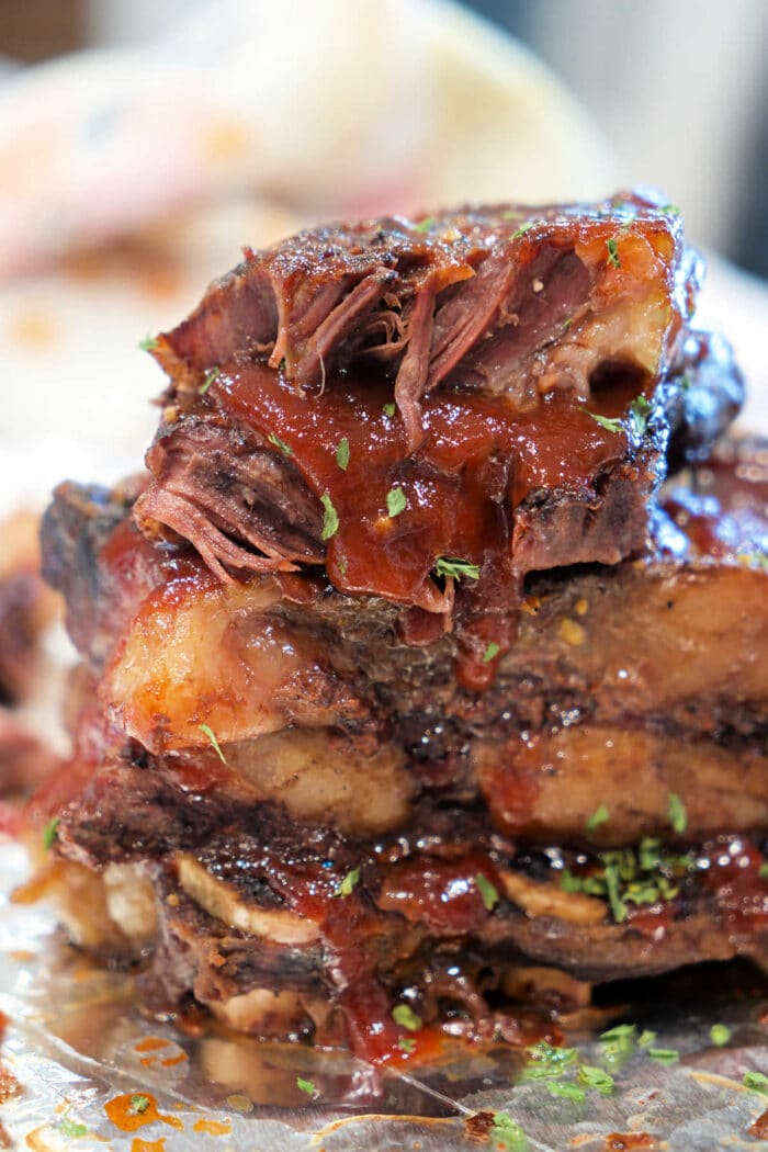 Close-up of stacked, juicy BBQ beef ribs with sauce and herbs on foil.