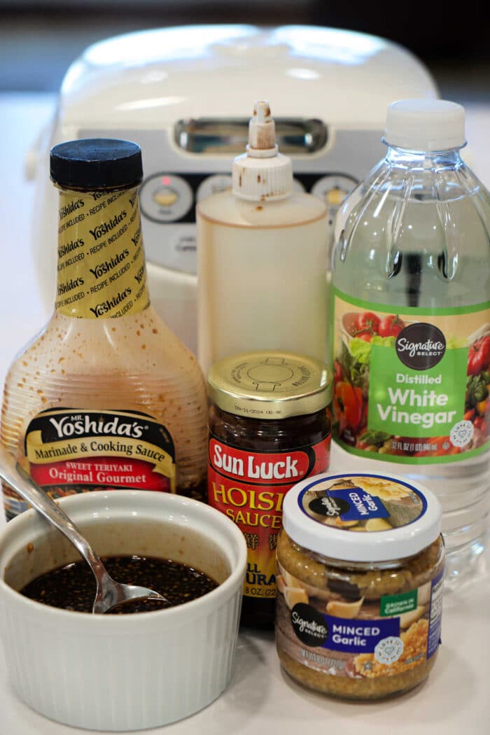 Various Asian sauces, minced garlic, vinegar, and a bowl of mixed sauce sit in front of a rice cooker—perfect accompaniments for Teriyaki Salmon Bites.