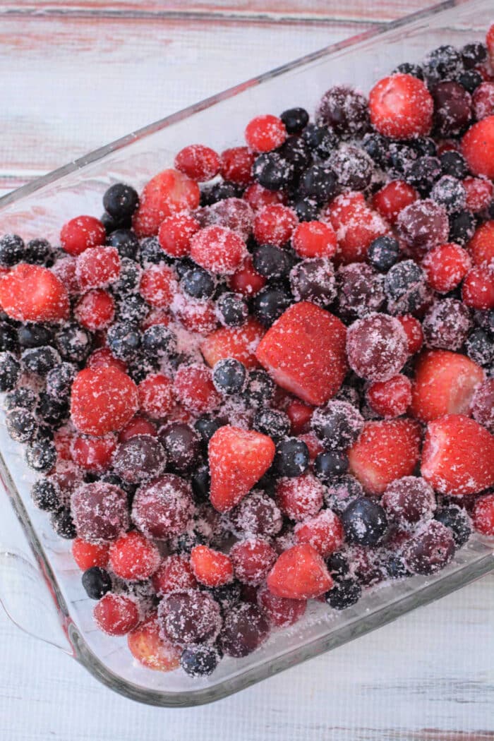 A glass dish filled with mixed frozen berries covered in sugar, ready to become a delicious Berry Cobbler with Cake Mix.
