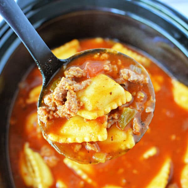 A ladle holds ravioli, ground beef, and tomato sauce over a Crockpot filled with the same mixture, creating a comforting Crockpot Lasagna Soup.