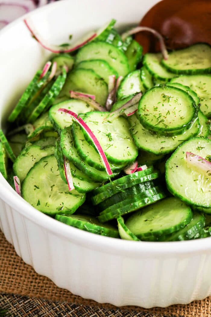Fresh cucumber salad with red onion and dill served in a white bowl.