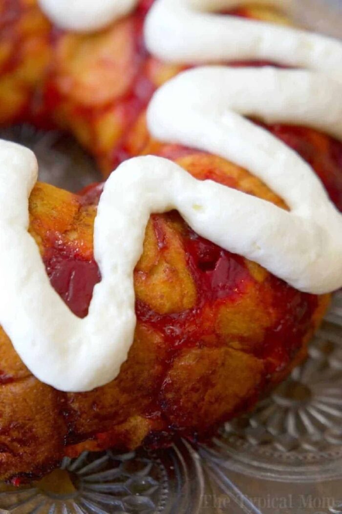 Close-up of a cherry cinnamon roll monkey bread ring topped with thick white icing on a glass plate.