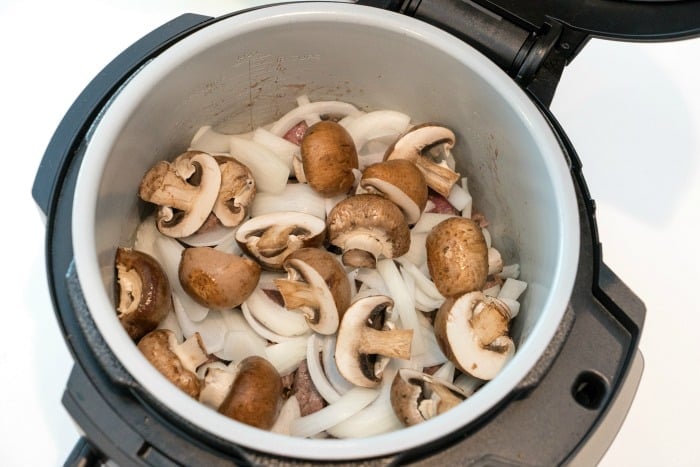 Sliced mushrooms and onions inside an open electric pressure cooker, perfect for making flavorful instant pot beef tips.