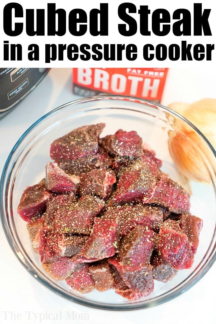 Raw cubed steak seasoned with pepper in a glass bowl, perfect for making instant pot beef tips, with broth and an onion in the background.