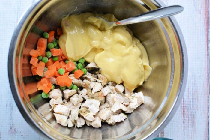 A mixing bowl with chopped chicken, frozen veggies, and creamy soup, just like in a classic KFC Chicken Pot Pie, with a spoon inside.