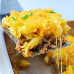 A spatula lifts a cheesy meatloaf casserole from a baking dish, topped with melted cheese and chives, blending classic casserole comfort with the creamy goodness of mac and cheese.