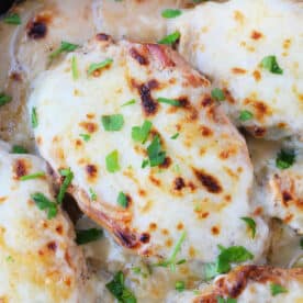 Chicken breasts topped with melted cheese and garnished with chopped parsley in a skillet, perfect for anyone who loves hearty dishes like Baked Pork Chops.