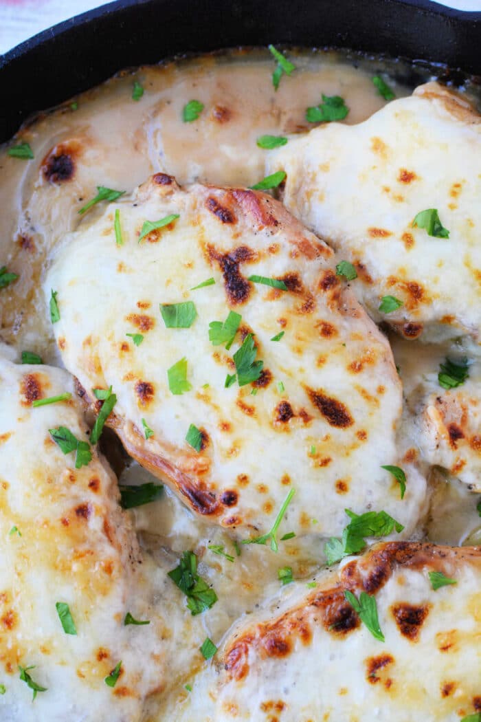 Chicken breasts topped with melted cheese and garnished with chopped parsley in a skillet, perfect for anyone who loves hearty dishes like Baked Pork Chops.