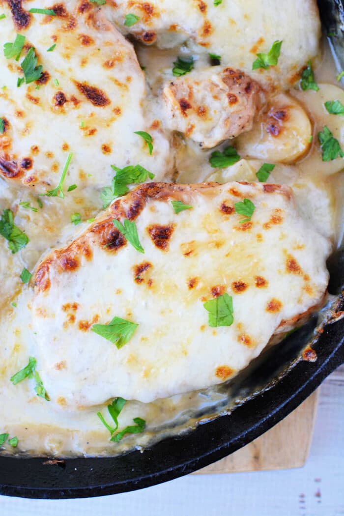 Chicken breasts in a creamy sauce, topped with melted cheese and fresh parsley in a skillet—try this technique with oven baked pork chops or pork chops with potatoes for a hearty twist.