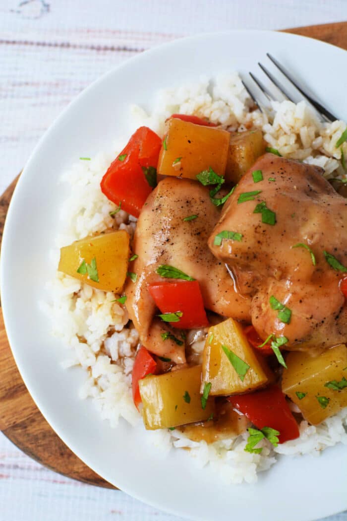 Slow Cooker Chicken with pineapple, red bell peppers, and savory sauce served over white rice on a white plate with a fork.