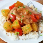 Slow Cooker Chicken with pineapple chunks and red bell peppers served over white rice on a white plate, finished with a splash of pineapple juice for extra flavor.