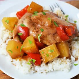 Slow Cooker Chicken with pineapple chunks and red bell peppers served over white rice on a white plate, finished with a splash of pineapple juice for extra flavor.