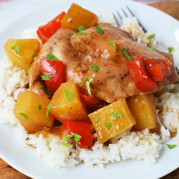 Slow Cooker Chicken with pineapple chunks and red bell peppers served over white rice on a white plate, finished with a splash of pineapple juice for extra flavor.