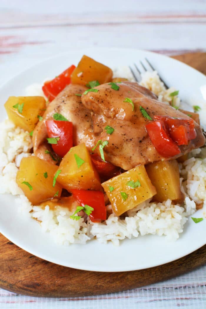 Slow Cooker Chicken with pineapple chunks and red bell peppers served over white rice on a white plate, finished with a splash of pineapple juice for extra flavor.
