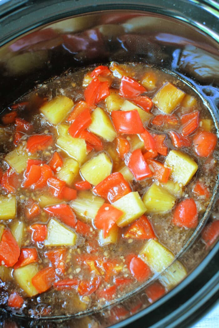 Diced red bell peppers, pineapple chunks, and tender slow cooker chicken simmer in a rich brown sauce for an easy chicken recipe.