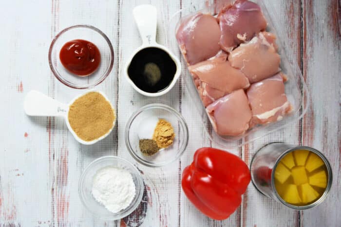 Raw chicken thighs, red bell pepper, canned pineapple, and small bowls of ketchup, spices, soy sauce, cornstarch, and a splash of pineapple juice—perfect for an easy Slow Cooker Chicken recipe.