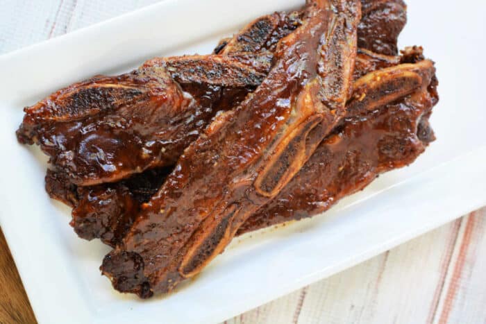 Grilled beef riblets with a shiny glaze, served on a rectangular white plate—a mouthwatering beef recipe perfect for any occasion.