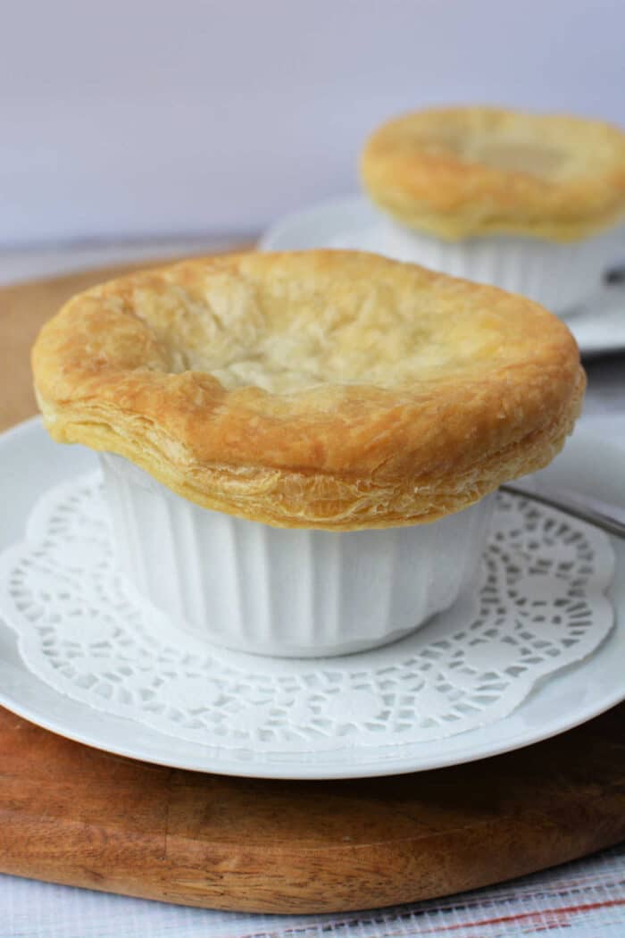 Golden puff pastry-topped KFC Chicken Pot Pie in a white ramekin on a plate with a doily and spoon.