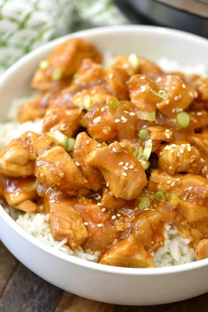 Spicy honey Instant Pot chicken takes just 4 minutes to cook and comes out moist and full of flavor! Sweet and spicy chicken bites smothered in delicious sauce which we love atop a bed of rice. A great healthy pressure cooker dinner our whole family enjoys. #instantpotrecipes #instantpot #pressurecooker #honey #chicken #spicy #thetypicalmom A bowl of white rice topped with spicy honey Instant Pot chicken, sliced green onions, and sesame seeds.