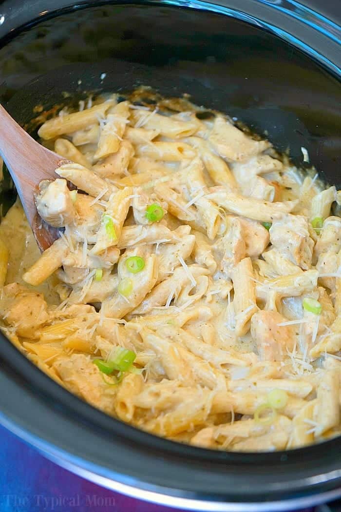 This easy crockpot pesto chicken alfredo casserole is a hit in my house! Cheesy noodles with moist pieces of pesto chicken together makes a complete meal. Creamy crockpot pesto chicken alfredo casserole with penne, cheese, and green onions, all blended together in a slow cooker with a wooden spoon.