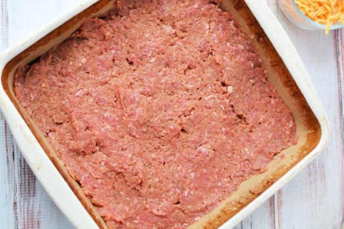 Raw ground meat mixture spread evenly in a square baking dish, ready to be cooked into a hearty meatloaf casserole.