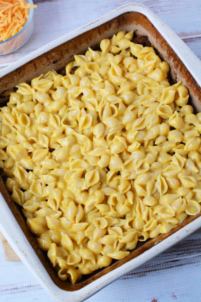 A baking dish filled with creamy mac and cheese made with shell pasta, ready to be baked into a delicious casserole.