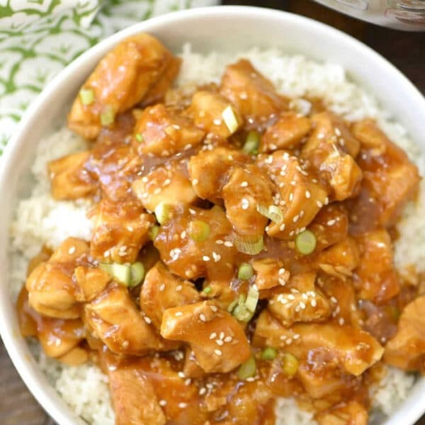 Bowl of rice topped with spicy honey Instant Pot chicken pieces, garnished with sesame seeds and sliced green onions.