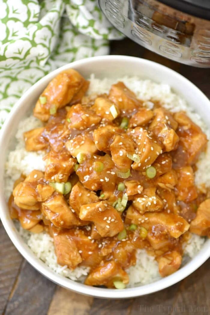 Spicy honey Instant Pot chicken takes just 4 minutes to cook and comes out moist and full of flavor! Sweet and spicy chicken bites smothered in delicious sauce which we love atop a bed of rice. A great healthy pressure cooker dinner our whole family enjoys. #instantpotrecipes #instantpot #pressurecooker #honey #chicken #spicy #thetypicalmom Bowl of rice topped with spicy honey Instant Pot chicken pieces, garnished with sesame seeds and sliced green onions.