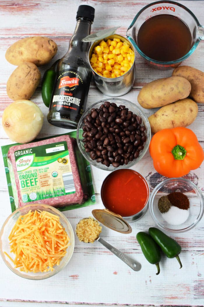 Ingredients for a Cowboy Casserole: potatoes, corn, black beans, cheese, beef, jalapeños, onion, spices, broth, and sauce—perfect for an easy Crockpot Tex-Mex meal.