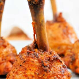 Close-up of seasoned, cooked Lollipop Chicken Drumsticks standing upright on a white plate.