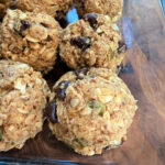 Close-up of homemade Peanut Butter Oatmeal Protein Balls with chocolate chips, seeds, and nuts in a glass dish.