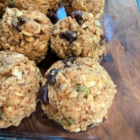 Close-up of homemade Peanut Butter Oatmeal Protein Balls with chocolate chips, seeds, and nuts in a glass dish.