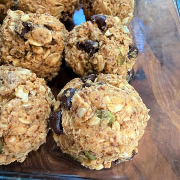 Close-up of homemade Peanut Butter Oatmeal Protein Balls with chocolate chips, seeds, and nuts in a glass dish.
