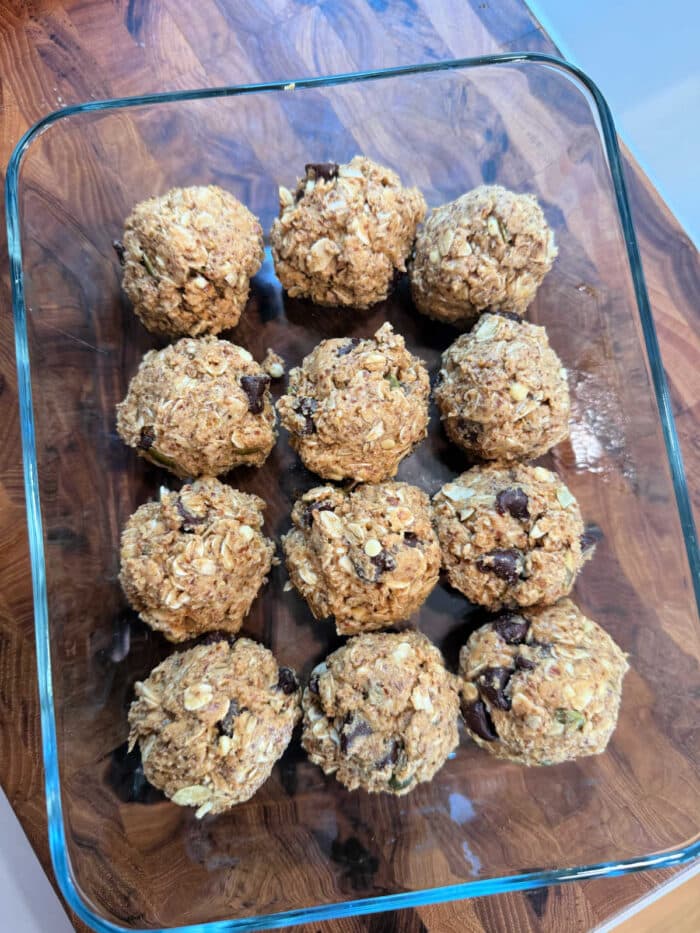 Twelve Peanut Butter Oatmeal Protein Balls with chocolate chips are arranged in a glass dish on a wooden surface.