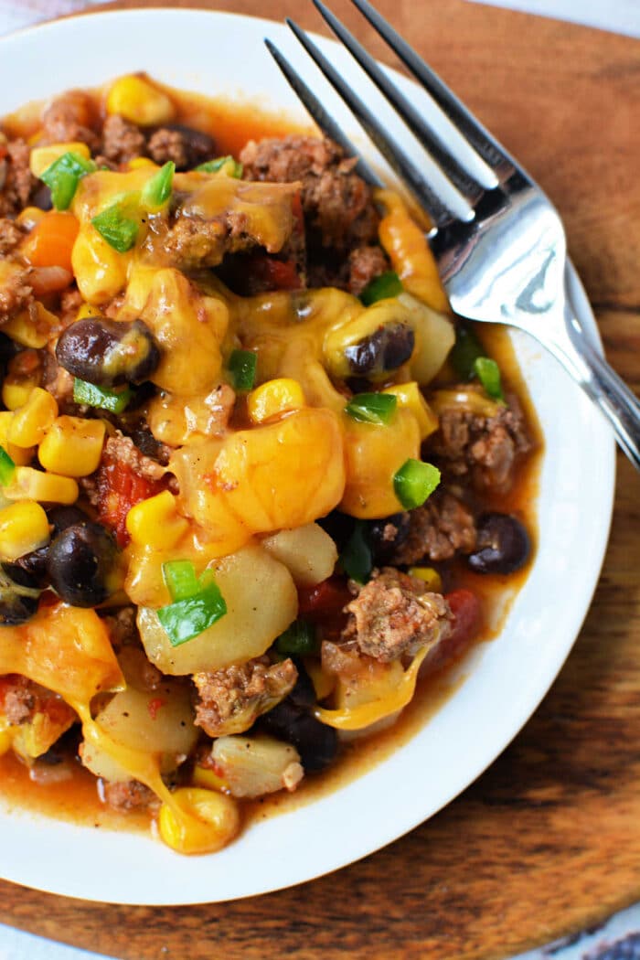 A plate of cheesy Cowboy Casserole with beef, black beans, corn, and potatoes sits next to a fork—perfect for fans of hearty Crockpot recipes.