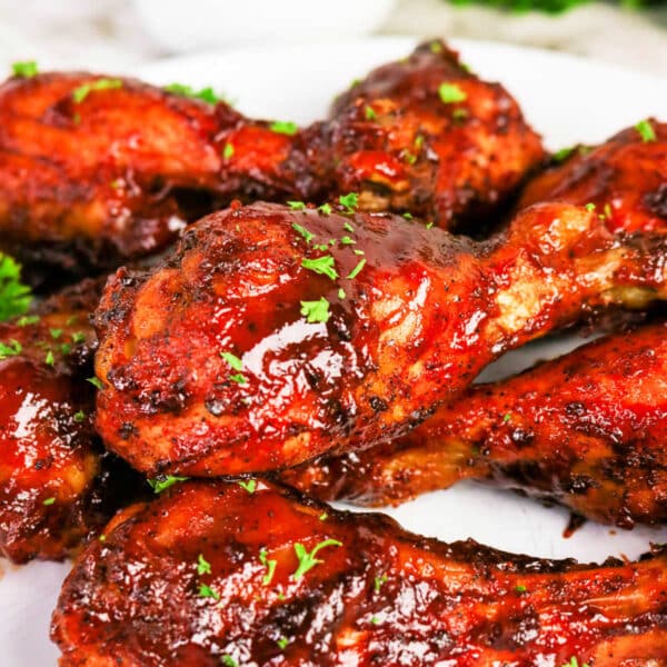 Oven baked BBQ chicken legs glazed with barbecue sauce and garnished with herbs, served on a white plate with sauce in the backgroundโa flavorful chicken recipe perfect for any occasion.
