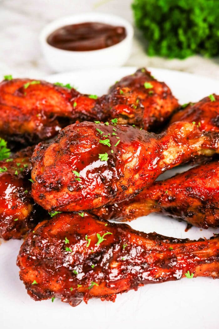Oven baked BBQ chicken legs glazed with barbecue sauce and garnished with herbs, served on a white plate with sauce in the background—a flavorful chicken recipe perfect for any occasion.