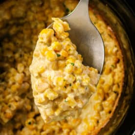 A spoon scooping creamy Crockpot Creamed Corn casserole from a slow cooker.