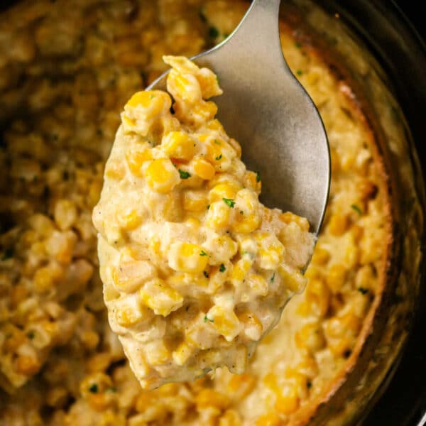 A spoon scooping creamy Crockpot Creamed Corn casserole from a slow cooker.