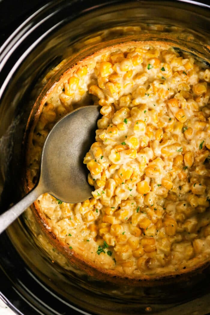 A spoon in a Crockpot filled with creamy cooked corn, garnished with herbs—perfect for savoring delicious Crockpot Creamed Corn.